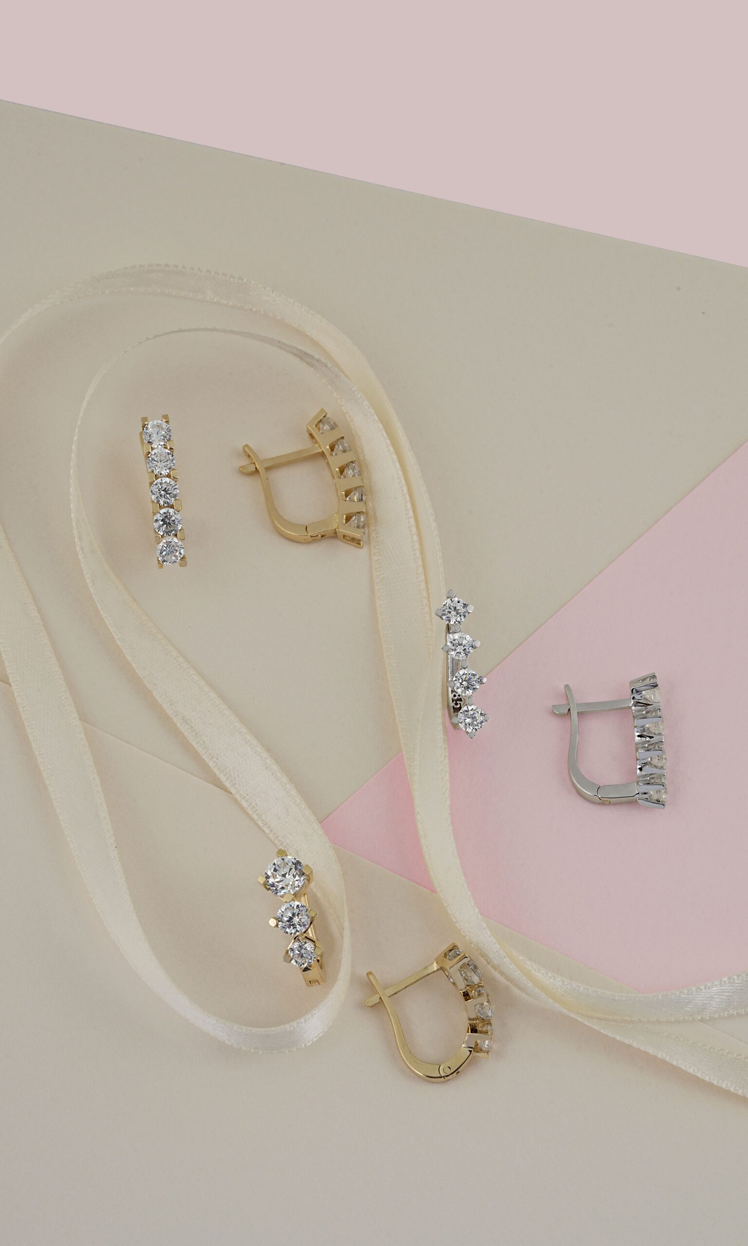 Elegant gold and silver earrings with diamonds on a pastel paper backdrop with ribbon.